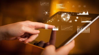 A person interacting with a tablet that projects digital graphs, charts, and a holographic globe above the screen, representing global data and technology.
