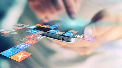 Close-up of a person's hand holding and interacting with a smartphone, surrounded by floating app icons representing various mobile applications, with a blurred background.