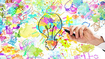 Hand drawing a light bulb with a black marker on a vibrant background filled with creative doodles, including charts, arrows, gears, and idea-related symbols.